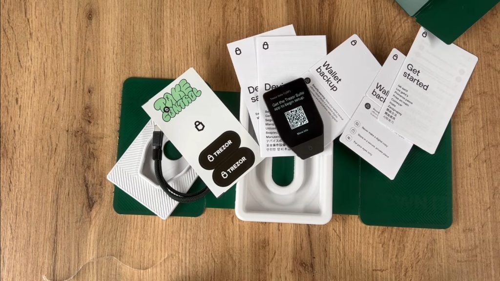 Trezor Safe 7 hardware wallet laid out beside its two backup cards, USB-C cable and start-up guide